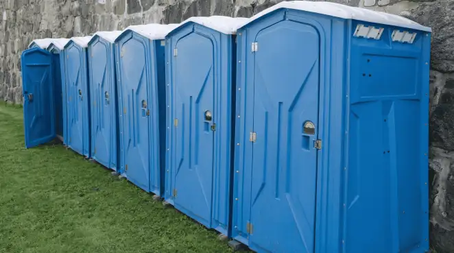 Row of blue portable toilets lined up on grass against a stone wall for event sanitation in Scottsdale, AZ